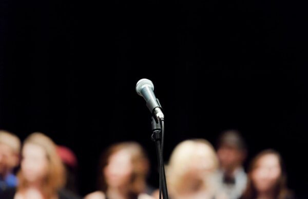 A wired silver microphone placed on a black mic stand in front of a blurry audience